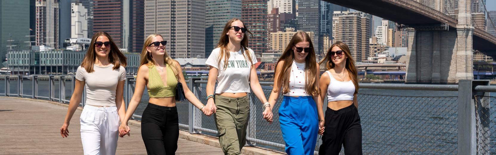fem au pairer går side om side i Manhattan med Brooklyn Bridge i baggrunden