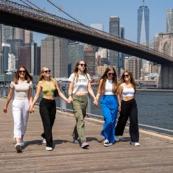 fem au pairer går side om side i Manhattan med Brooklyn Bridge i baggrunden